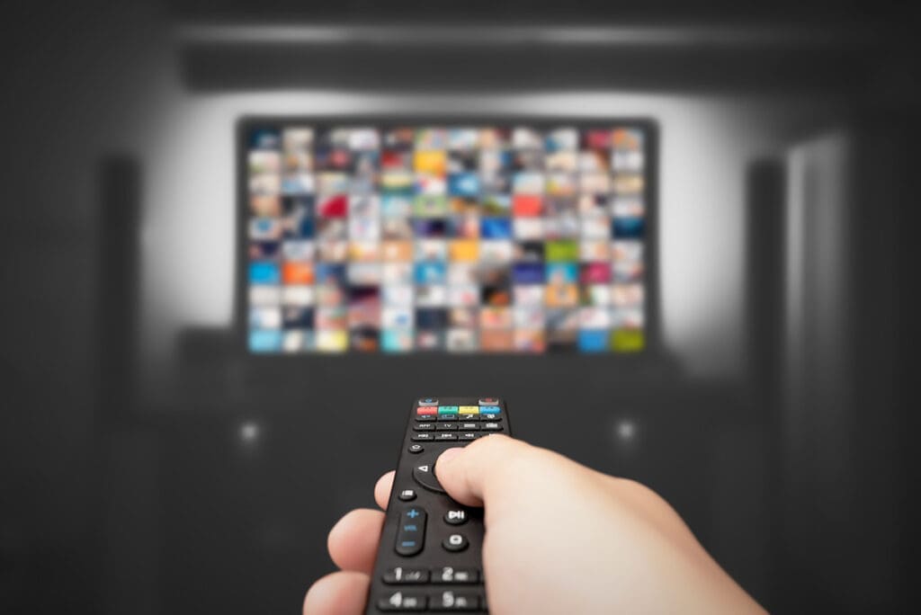 Hand Points Remote Control at Large Selection of Content on Television