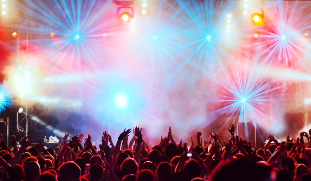 People at a concert in front of colorful lights and flashing lights, in the style of light red and dark cyan, vibrant fantasies, award-winning, abrasive authenticity, eye-catching