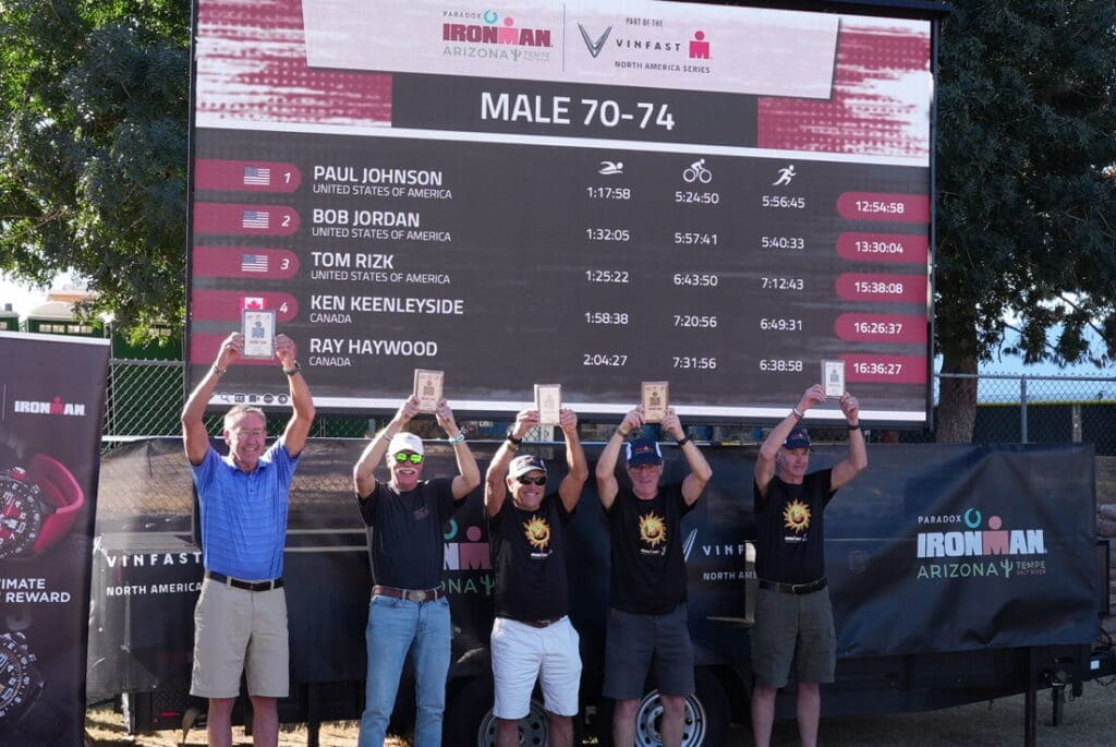 A Mobile LED screen with 5 people in front of it holding up their awards. The screen shows the top five participants in the 70-74 age group at IRONMAN Arizona.