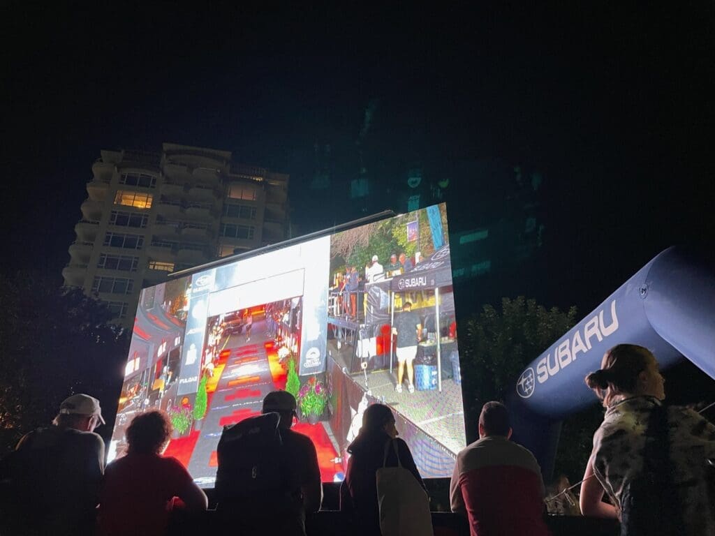 A group of people gathered in front of an LED screen, engrossed in watching the content displayed. The LED screen emits bright, vibrant colors, captivating the attention of the viewers.